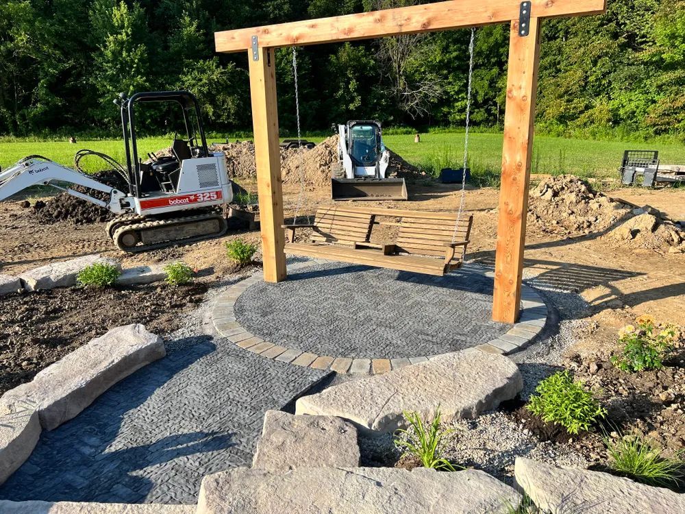 A wooden swing is sitting in the middle of a garden with a bulldozer in the background.