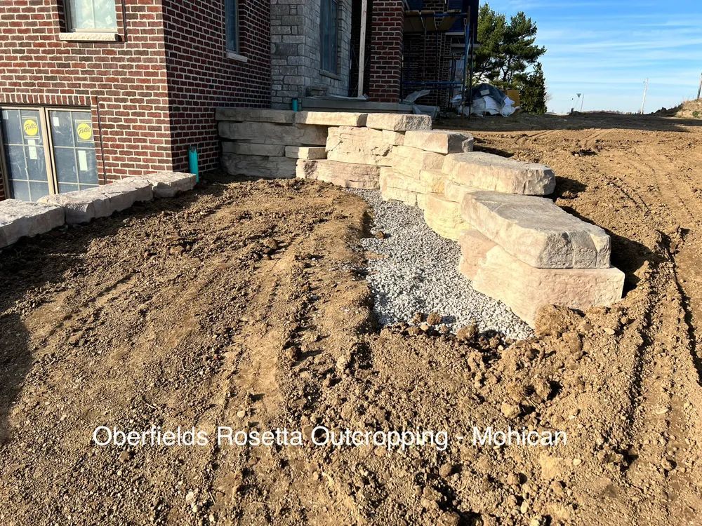 A brick house is being built in the middle of a dirt field.