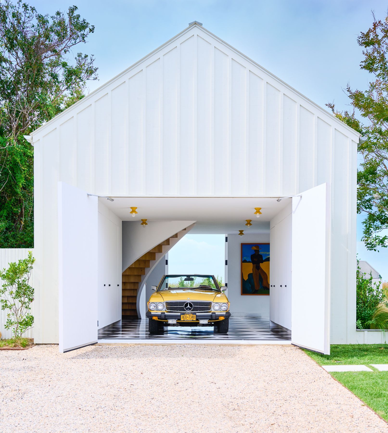 White garage with open doors, yellow convertible, and a spiral staircase.