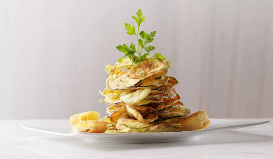 Fried zucchini and potatoes stacked on a white plate, garnished with parsley.