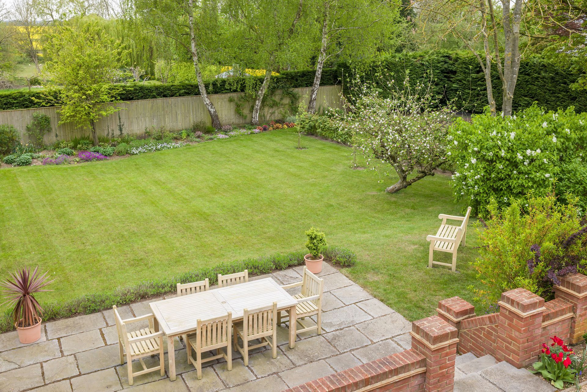 Backyard with a manicured lawn, patio dining set, and a single chair near trees and shrubs