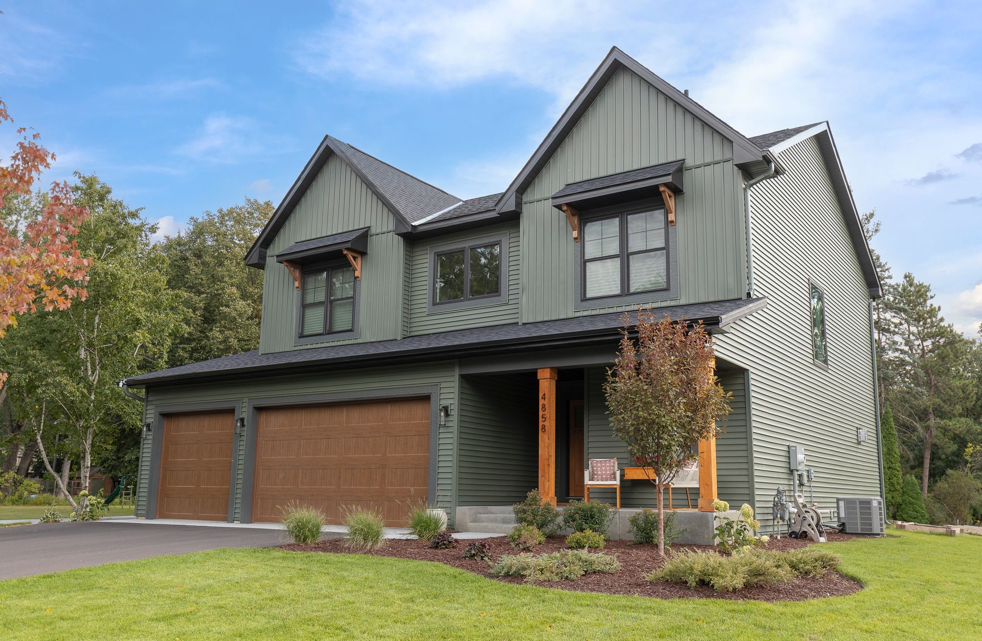 Two-story house with gray siding, brown garage doors, and a green lawn under a blue sky