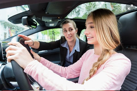 Stock photo of a driving instructor teaching a young person to drive in a car.