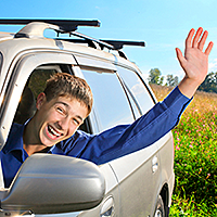 Stock photo of a young man smiling and waving out of the car
