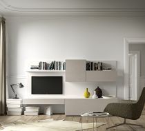 Un mobile a parete minimalista, color bianco sporco, con televisore a incasso, ripiani per libri, lampada e oggetti decorativi, accanto a una poltrona.