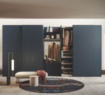 Un armadio modulare blu scuro con ripiani a giorno e chiusi, posizionato dietro una panca beige su un tappeto circolare a motivi geometrici.