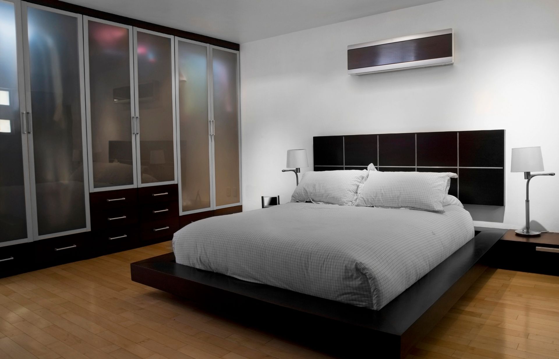 Una camera da letto moderna con letto a piattaforma, mobili in legno scuro, armadi con ante in vetro satinato e una parete bianca con condizionatore d'aria.