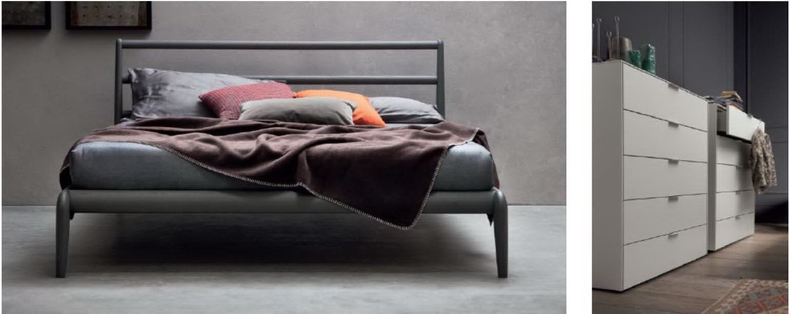 Un letto con struttura in metallo grigio scuro e coperte sovrapposte si trova accanto a una cassettiera alta e moderna di colore bianco, dotata di numerosi cassetti.