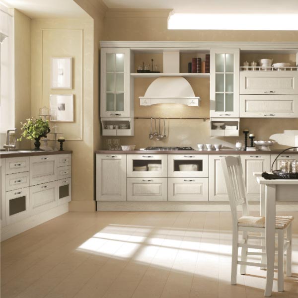 Una cucina classica con mobili color avorio sporco, una cappa decorativa e pavimenti in legno chiaro, inondata di luce naturale.