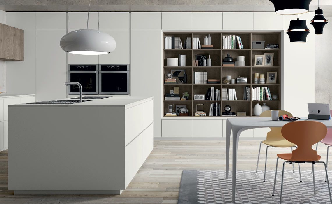 Una cucina moderna ed elegante con isola bianca, pensili alti, libreria a muro e zona pranzo con sedie colorate.