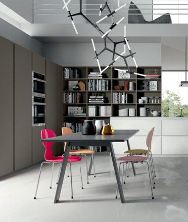 Cucina moderna con tavolo da pranzo grigio scuro, quattro sedie colorate e una libreria a tutta altezza con una lampada dal design particolare.