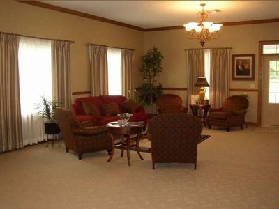 Bright living room with beige carpet, red sofa, armchairs, curtains, and a chandelier