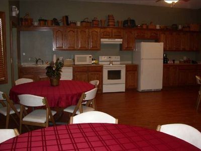Kitchen and dining area with wooden cabinets, white appliances, and tables covered in red tablecloths.