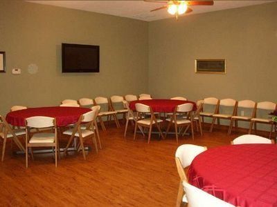 Empty banquet room with round tables covered in red tablecloths and rows of chairs along the wall.