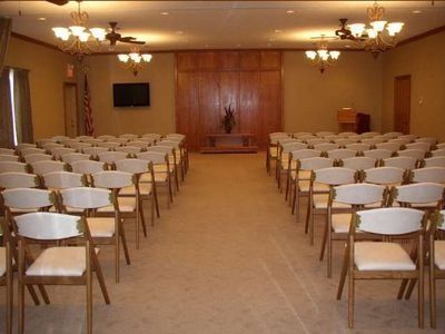 Empty meeting room with rows of chairs facing a wood-paneled stage and podium.