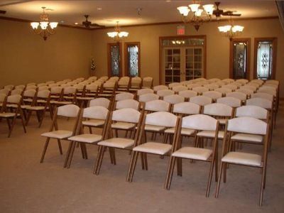 Empty banquet hall with rows of white folding chairs under warm ceiling lights