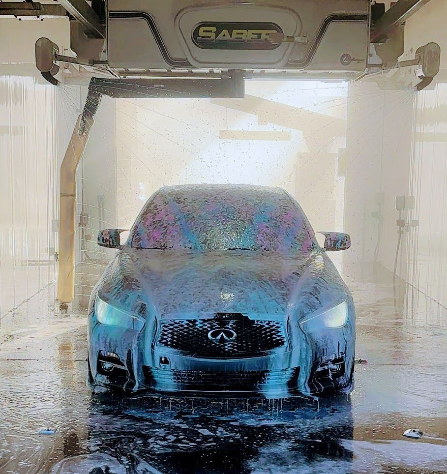 Car at car wash, covered in soapy foam, under Saber machine.