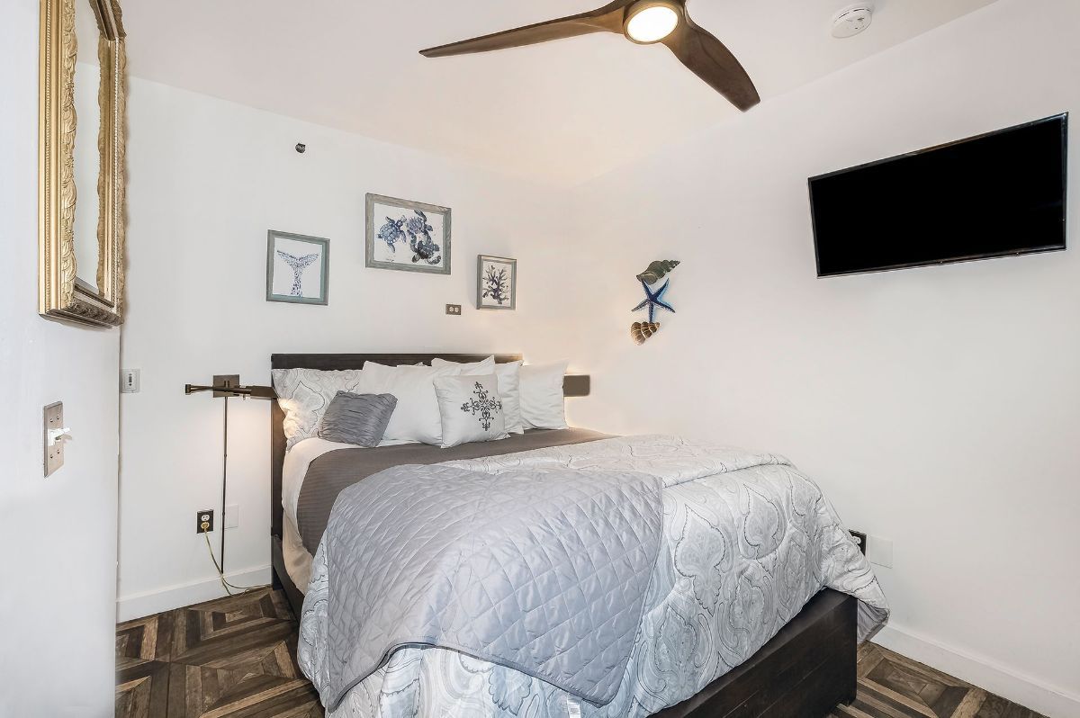a bedroom with a bed , ceiling fan , television and mirror .
