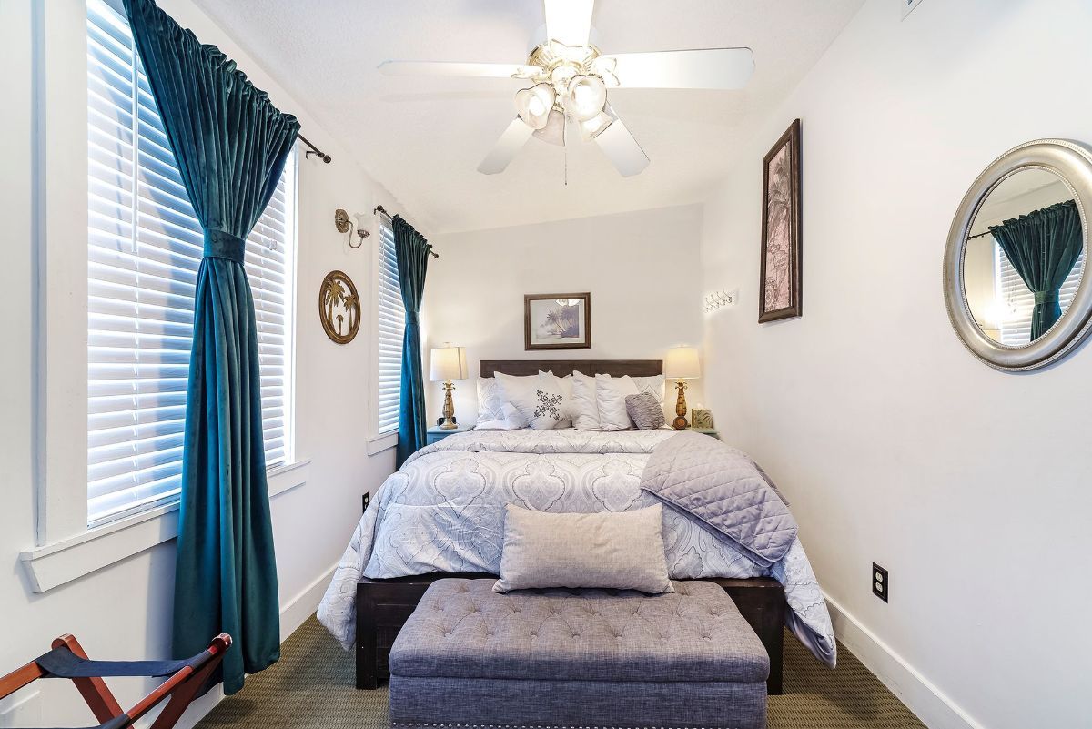 a bedroom with a bed , ottoman , mirror and ceiling fan .