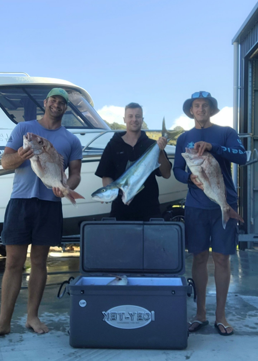 Three people holding freshly caught fish in front of a boat and a cooler.