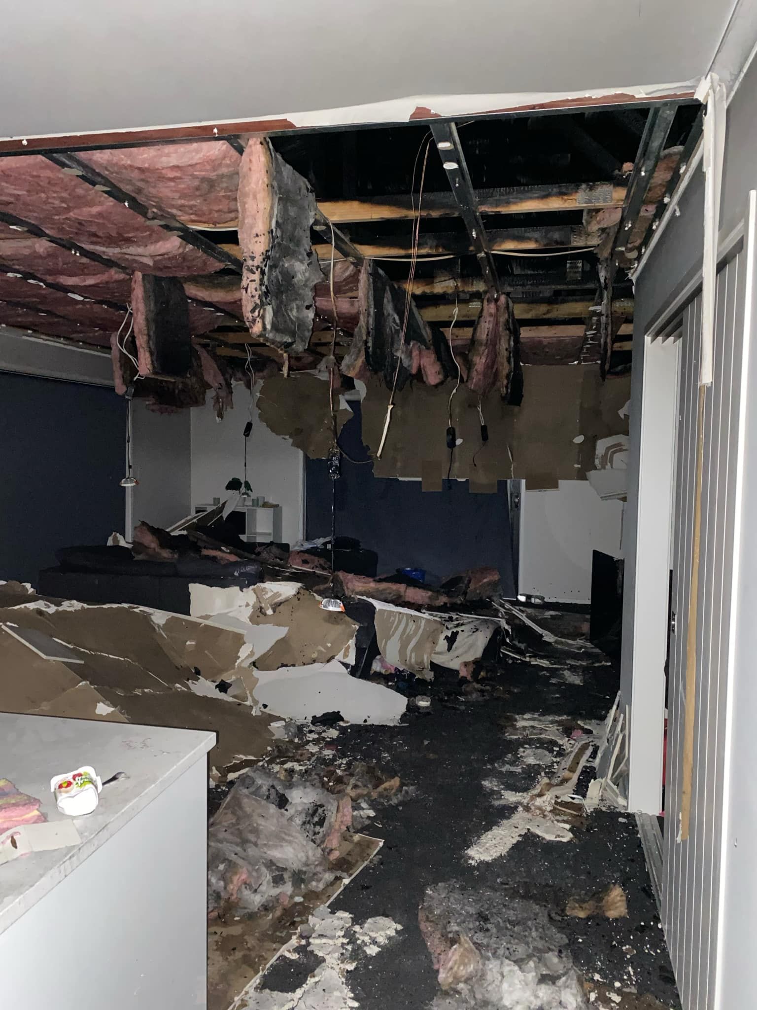 Interior of a room with a collapsed ceiling, exposed insulation, and fire damage throughout the space.