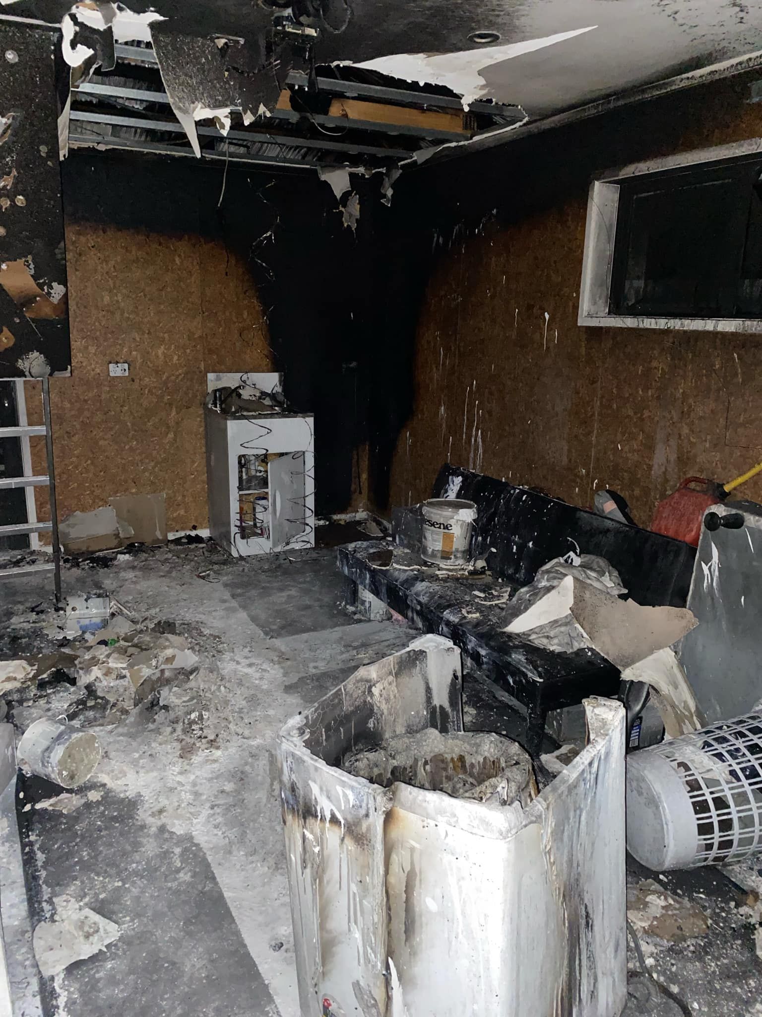 A room damaged by fire with charred walls, a ruined ceiling, and debris scattered across the floor.