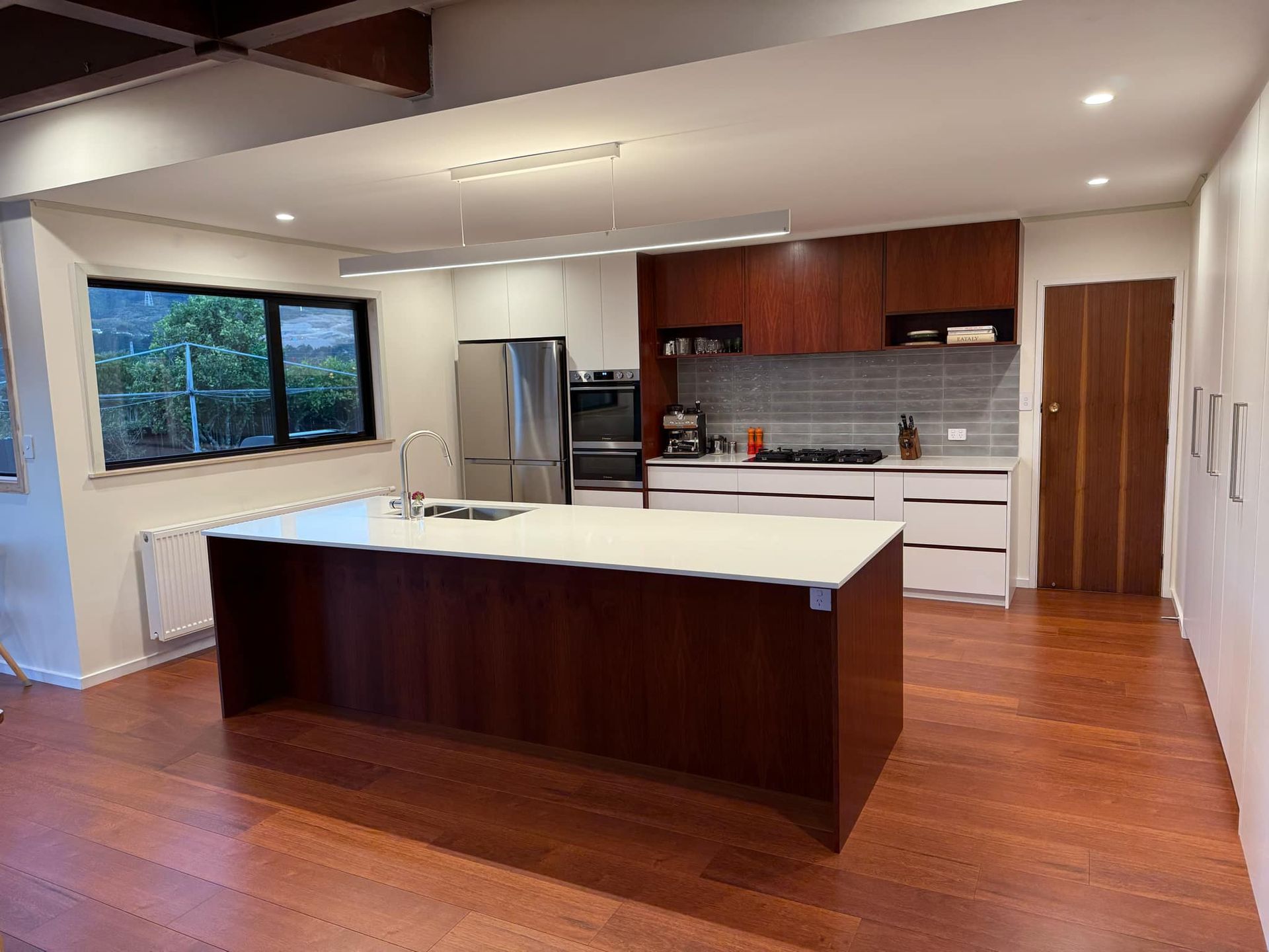 Modern kitchen with a large dark wood island, white countertops, stainless steel appliances, and rich wood flooring.