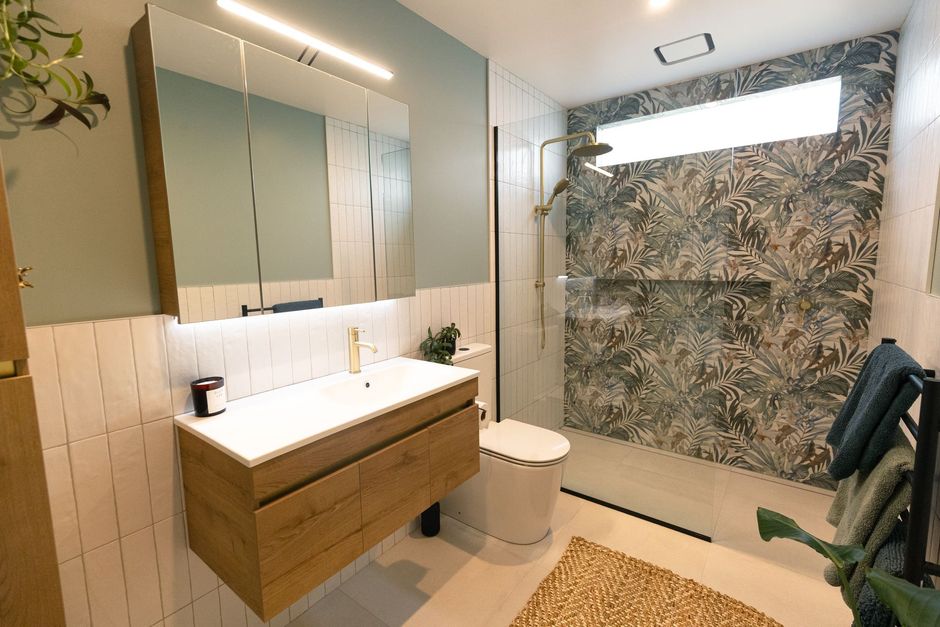 Modern bathroom featuring a wood vanity, green wall, patterned tile shower, and a large mirror with integrated lighting.