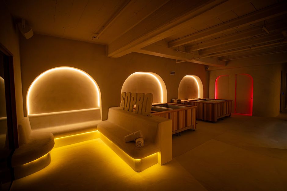 A dimly lit lounge with warm gold-toned lighting, recessed arched seating, and textured walls.