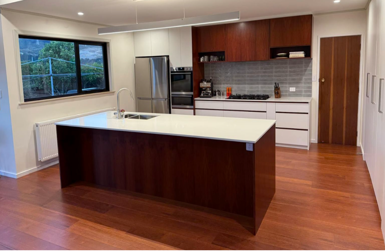 A modern kitchen featuring a central island with a white countertop, dark wood cabinets, stainless appliances, and floors.