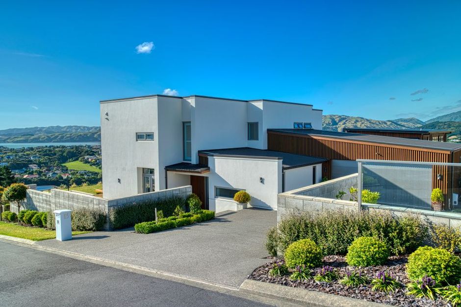 Modern, white multi-level house with brown accents, a gravel driveway, and landscaped garden against a coastal backdrop.