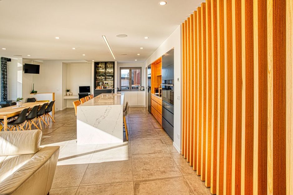 Modern open-plan kitchen featuring a large marble island, wood slat wall, and adjacent dining area with tile flooring.