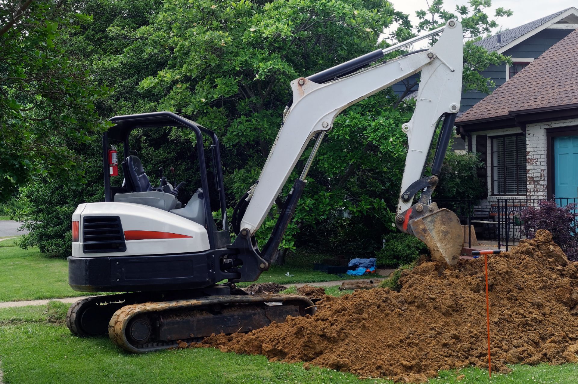 Une petite pelleteuse creuse dans le jardin d'une maison, créant un tas de terre brune.