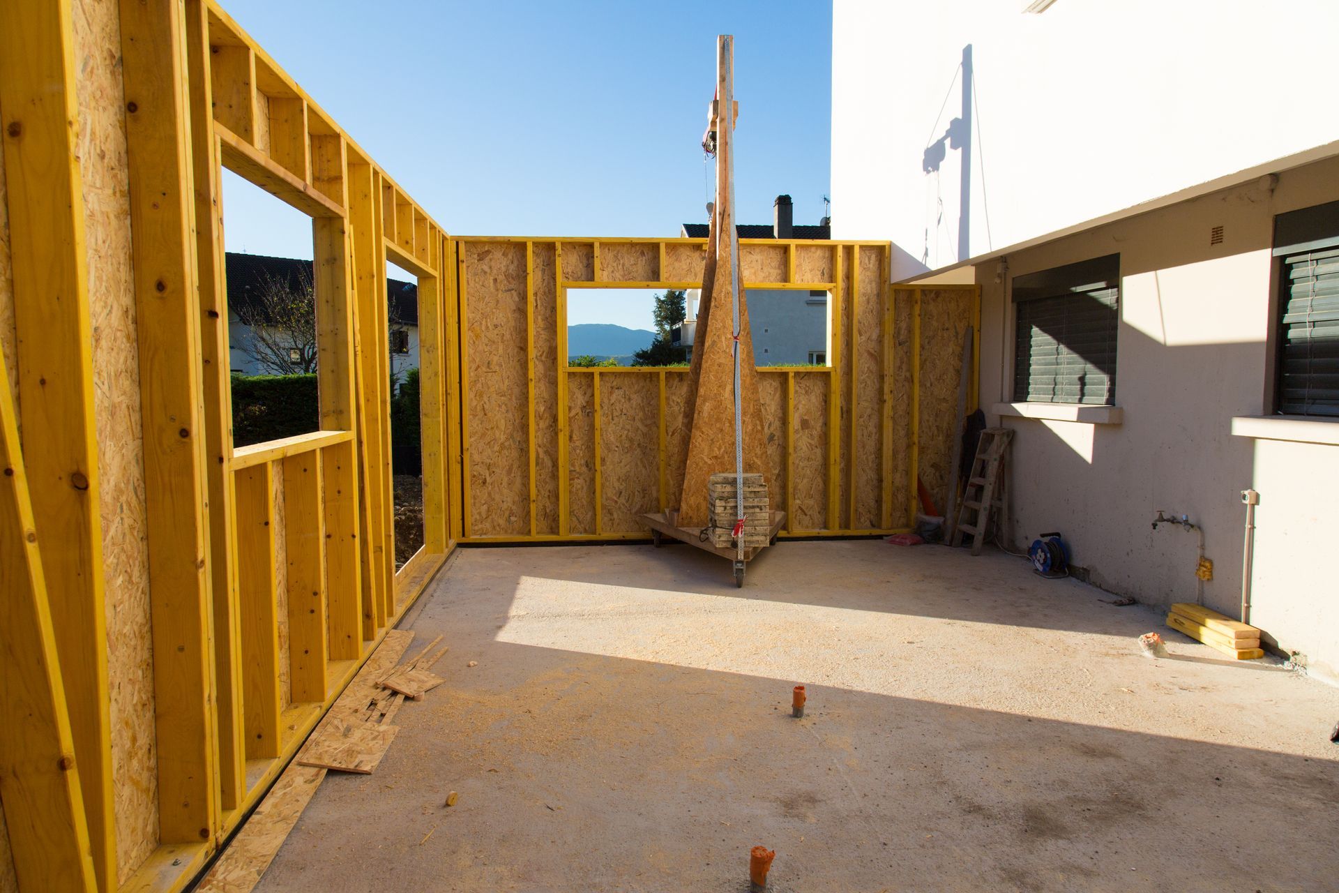 Chantier : Ossature bois avec ouvertures pour fenêtres, sol en béton, cadre extérieur ensoleillé.