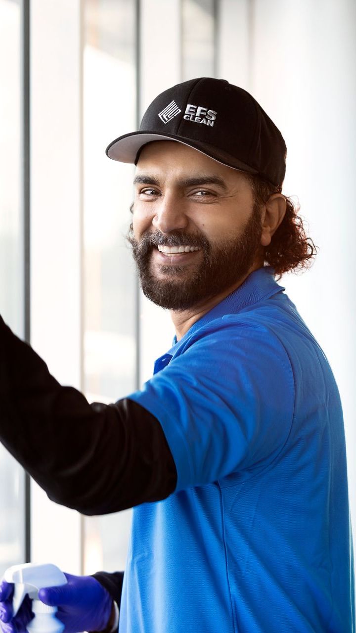 A man wearing a blue shirt and a black hat is cleaning a window.