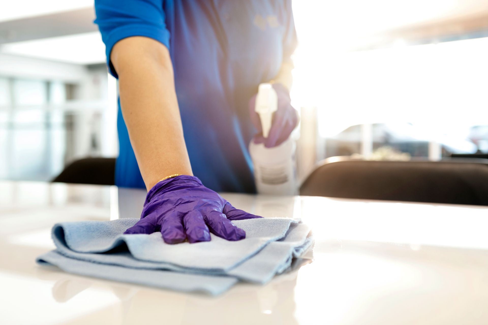 A person wearing purple gloves is cleaning a table with a cloth.