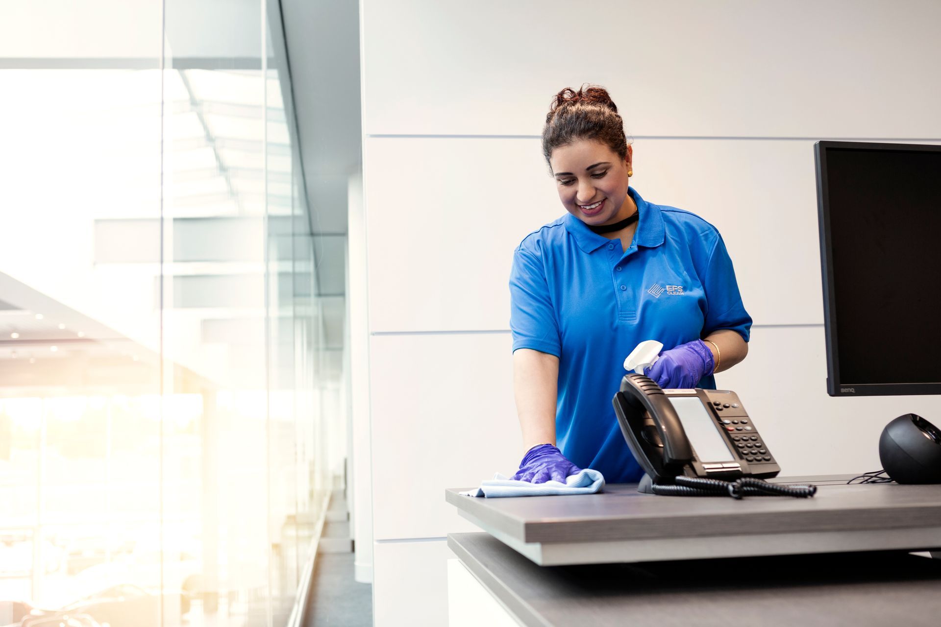 A woman in a blue shirt is cleaning a phone on a desk.