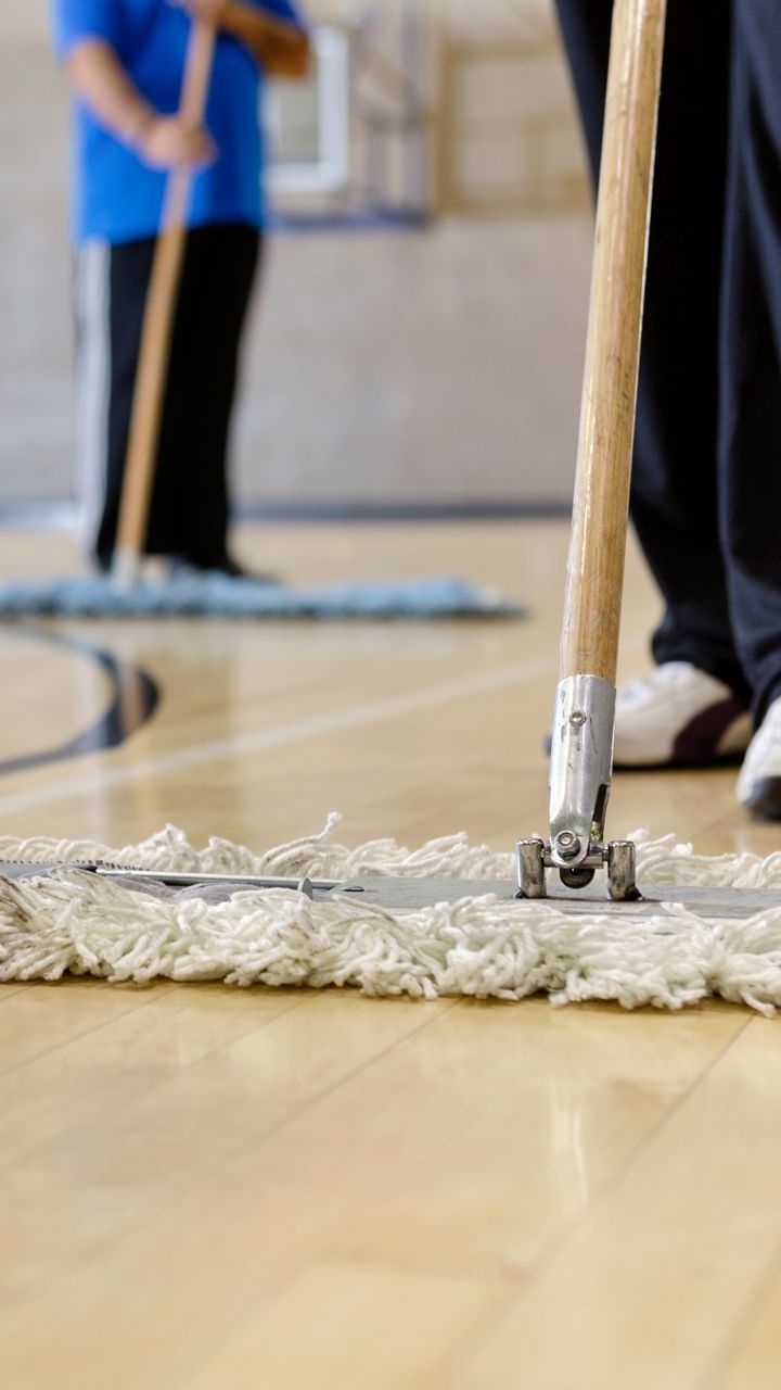 Two people mopping a wooden basketball court with white mops.