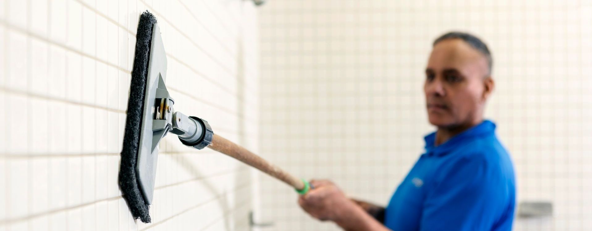 A man in a blue shirt is cleaning a tiled wall with a mop.