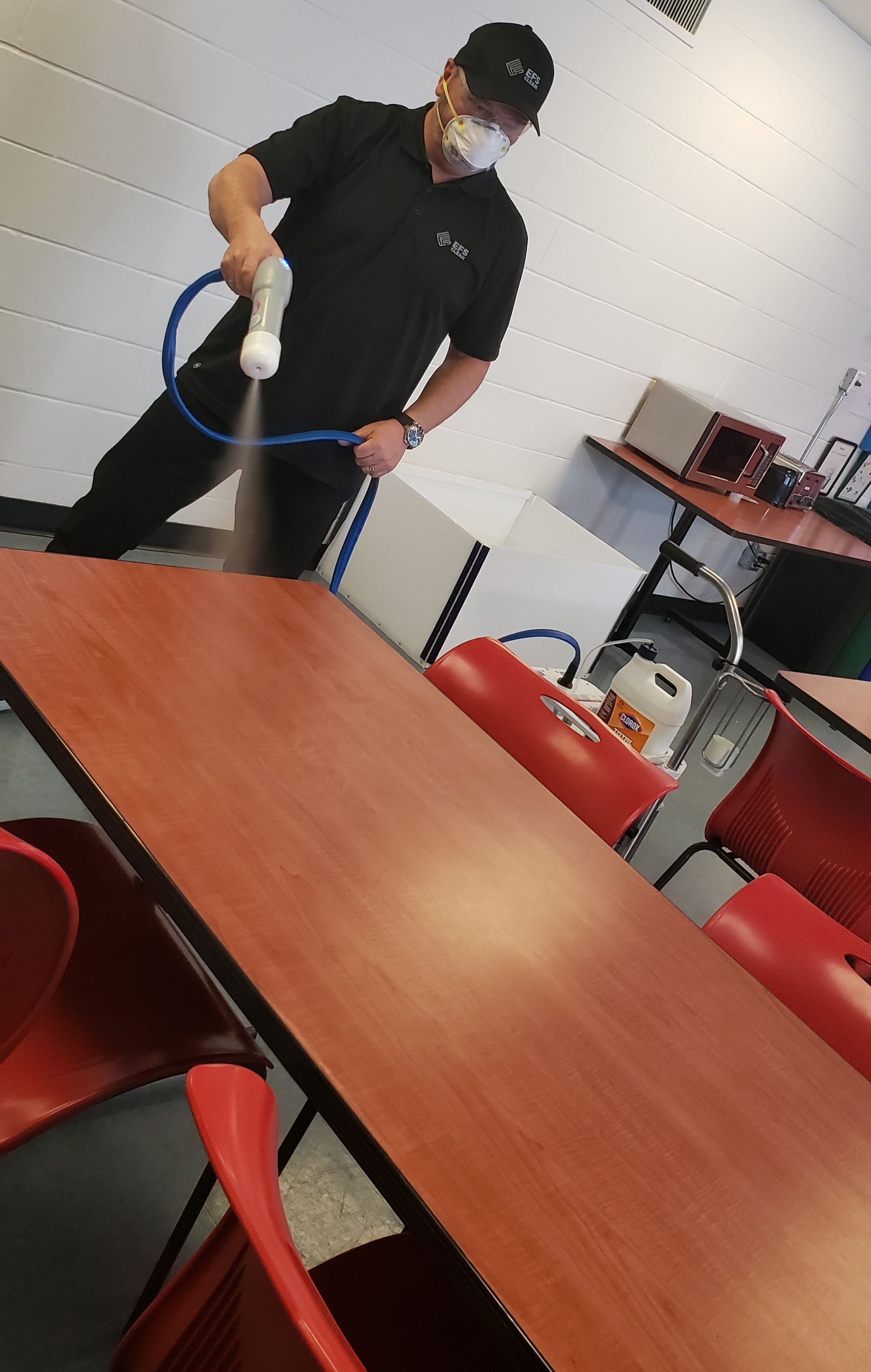 A man wearing a mask is spraying a table with a hose.