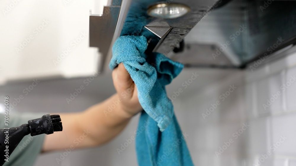 A person is cleaning a kitchen hood with a blue towel.