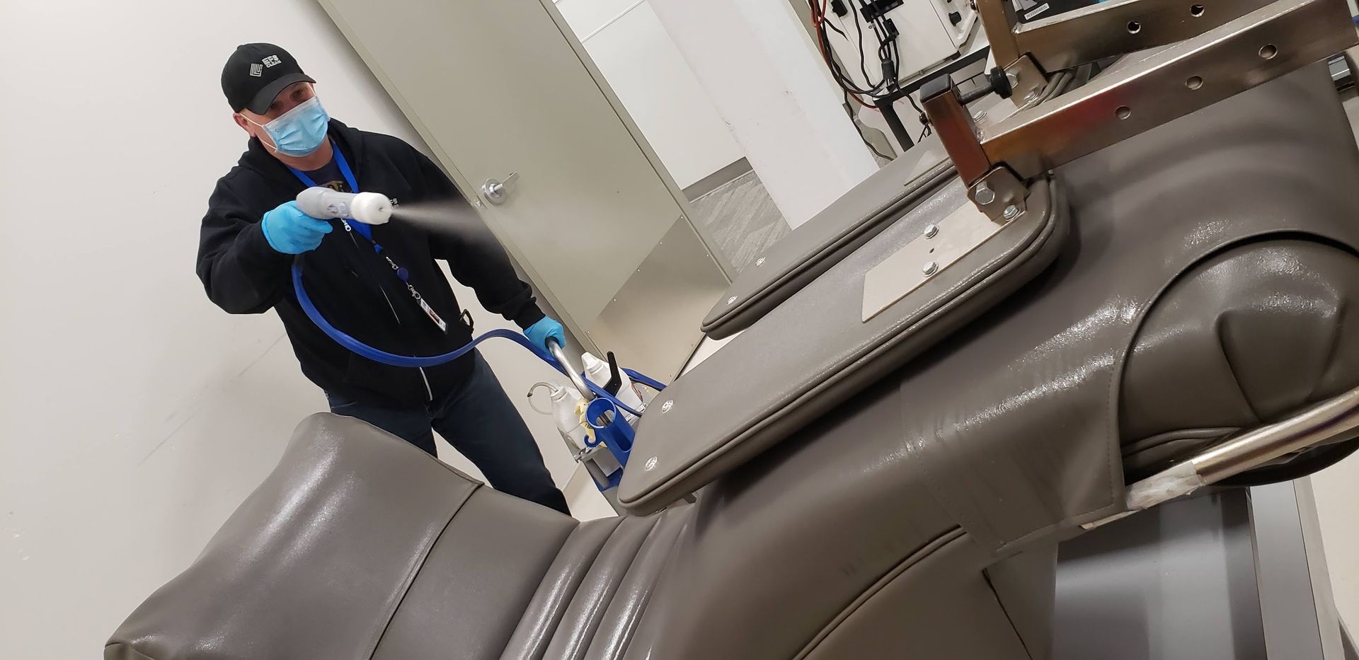 A man wearing a mask and gloves is spraying a chair with a hose.