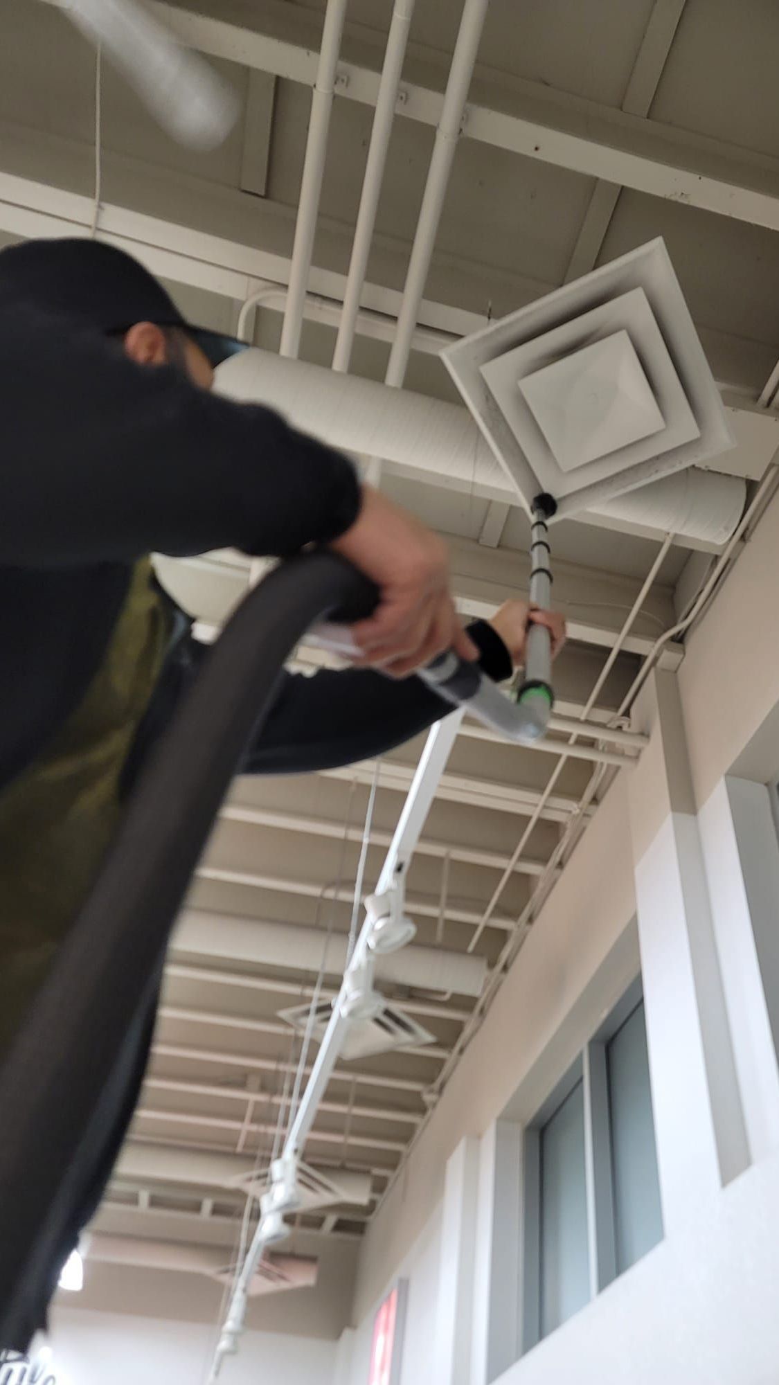 A man is using a vacuum cleaner to clean the ceiling of a building.