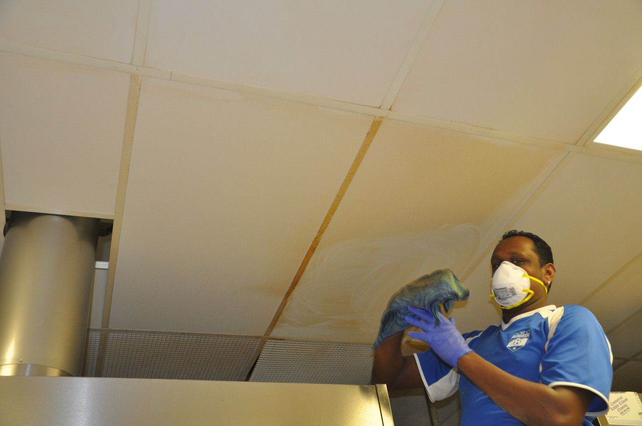 Person wearing a mask and gloves cleans a commercial ceiling.