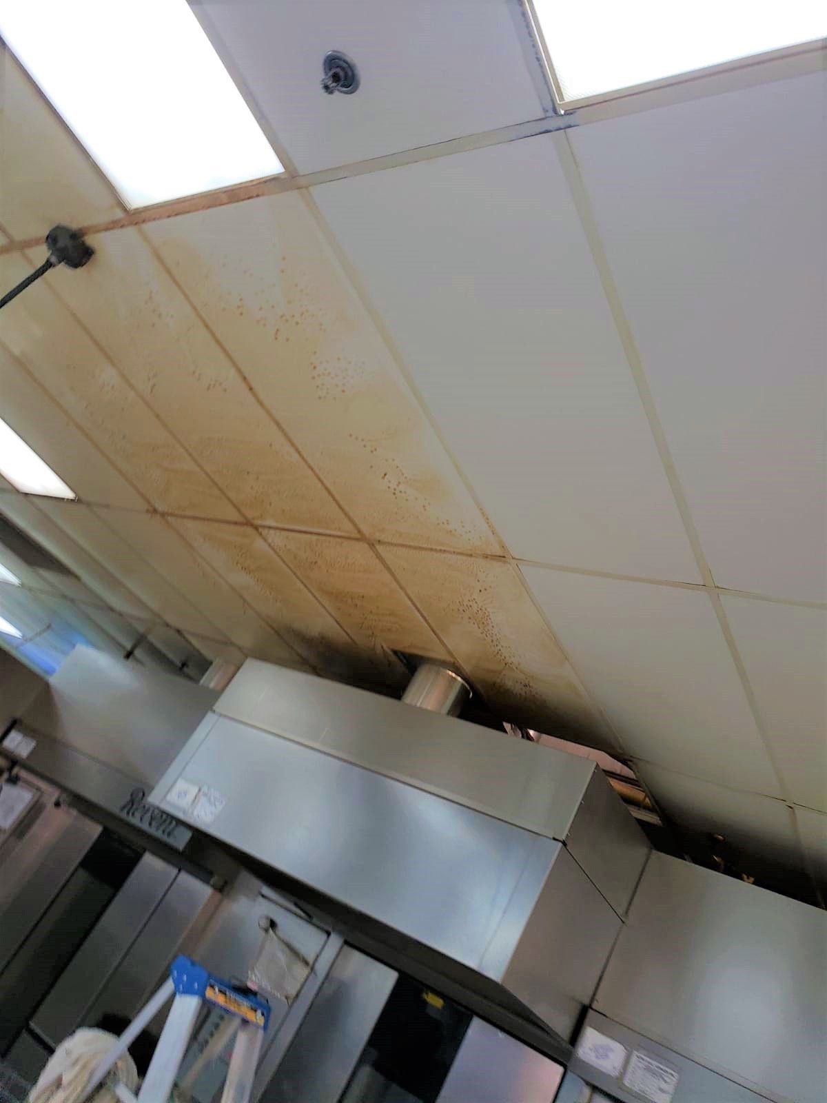 A kitchen with a dirty ceiling and a ladder.
