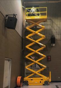 A man is standing on a yellow scissor lift.
