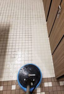 A vacuum cleaner is cleaning a tiled floor in a bathroom.