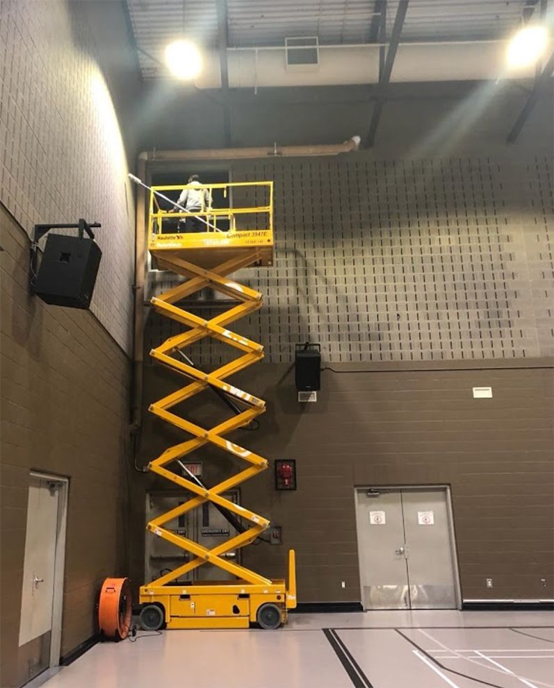 A man is standing on a scissor lift in a gym.