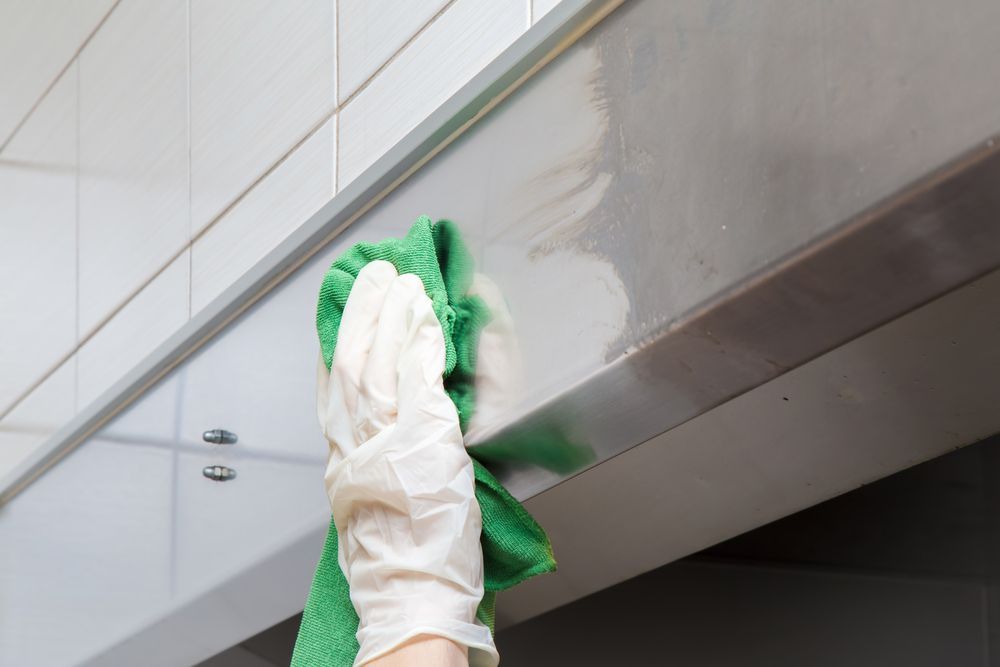 A person is cleaning a stainless steel cabinet with a green towel.