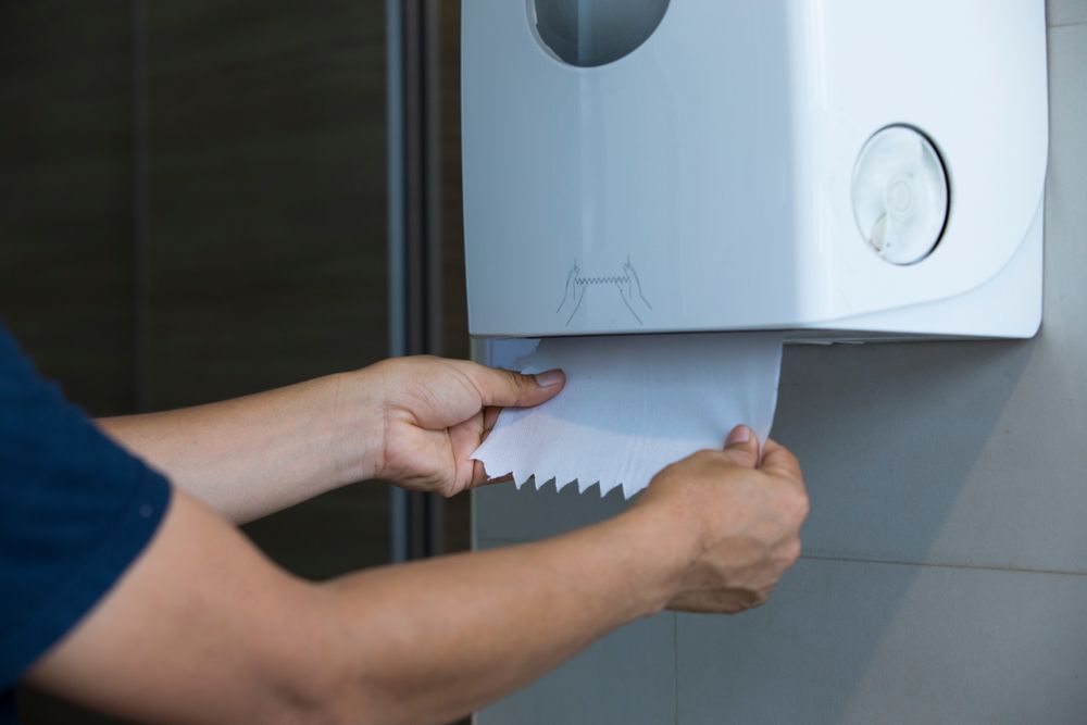A person is taking a roll of toilet paper out of a paper towel dispenser.